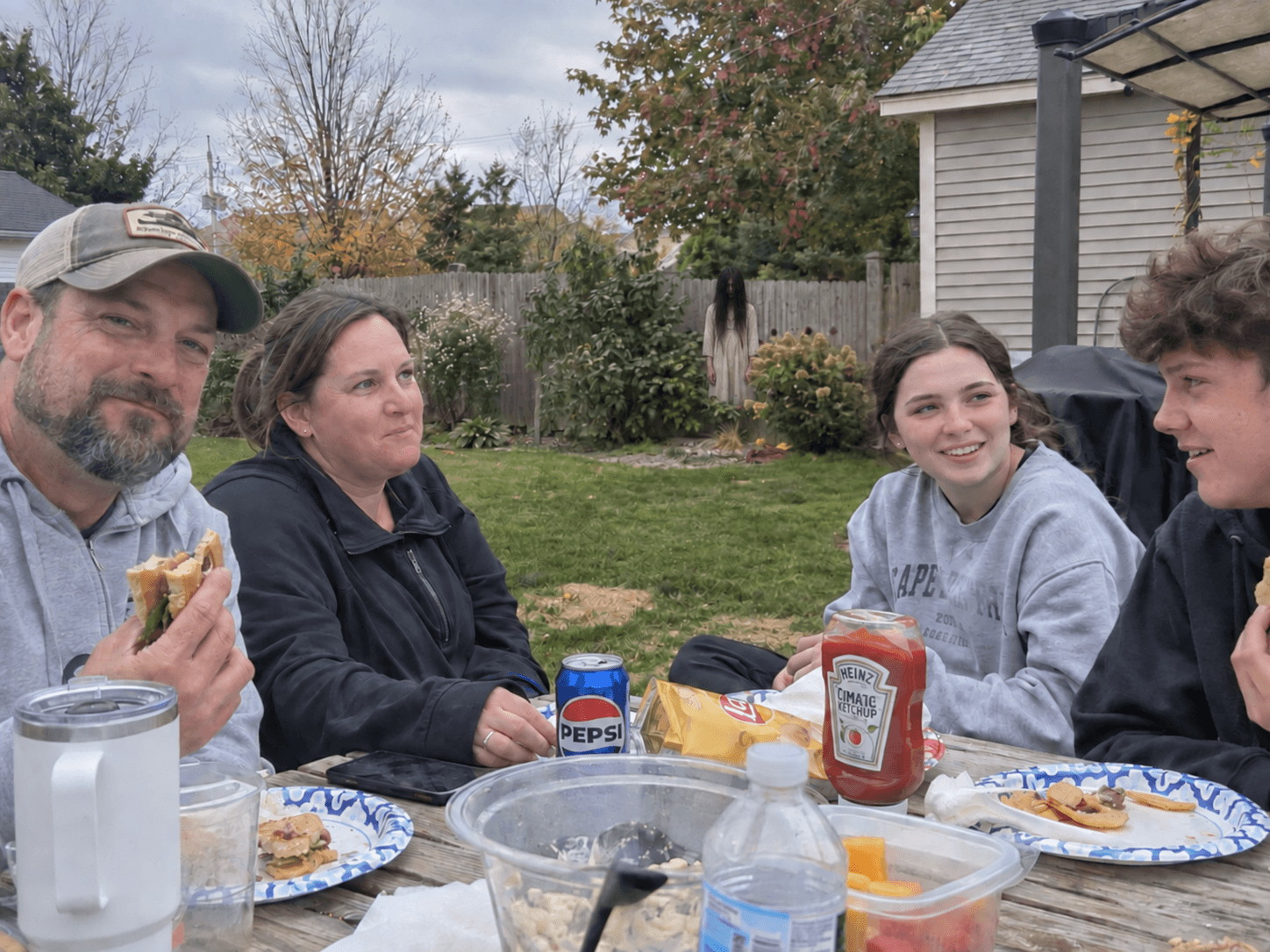 The same family lunch with a long-haired watcher beside the back fence